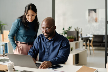 Asian Woman And Black Man Looking At Laptop Screen - Powered by Adobe