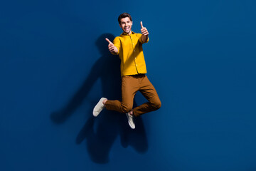 Fototapeta na wymiar Full size photo of handsome young man jump show thumb up good quality wear trendy yellow outfit isolated on dark blue color background