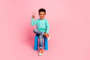 Full length photo of adorable little boy sit chair show v-sign wear trendy aquamarine garment...