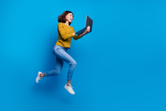 Full length photo of positive cute woman wear shirt jumping running working modern device empty space isolated blue color background