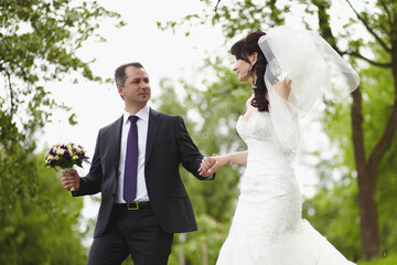 The bride and groom walk through the park on a summer day