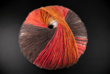 A ball of yarn with orange and brown stripes. The yarn is sitting on a black surface. The yarn is colorful and has a unique pattern