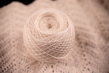 Ball of yarn is sitting on piece of lace. Yarn is white and lace is light color. Yarn is unspun and ready to be used for knitting or crocheting