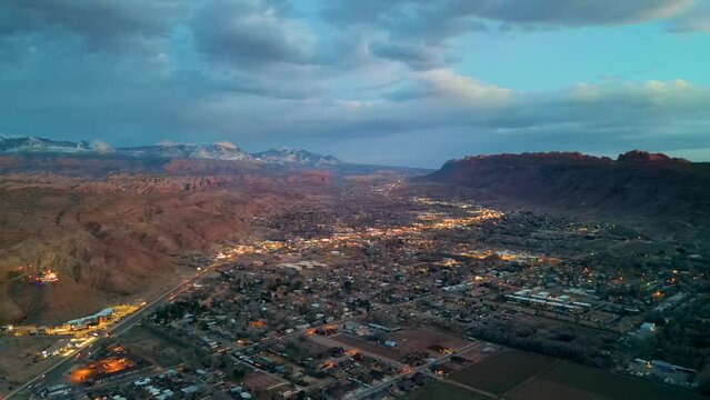 aerial shot of moab utah with red mountains behind the city during sunset