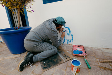 Caucasian adult man painting decorative cats on a tourist house building