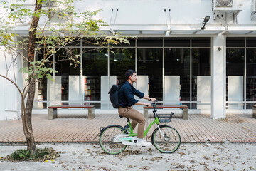 Young businessman ride bicycle to work to reduce global warming through the park. Eco friendly...