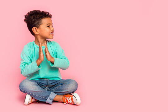 Full length photo of adorable little boy sit floor clap look empty space wear trendy aquamarine garment isolated on pink color background