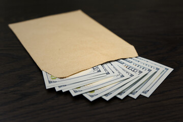 An open brown envelope, crafted from recycled paper, lies atop a stack of US hundred-dollar bills...