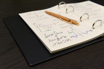 An open notebook reveals intricate mathematical equations and colorful graphs, accompanied by a luxurious golden pen, suggesting a moment of deep academic engagement.
