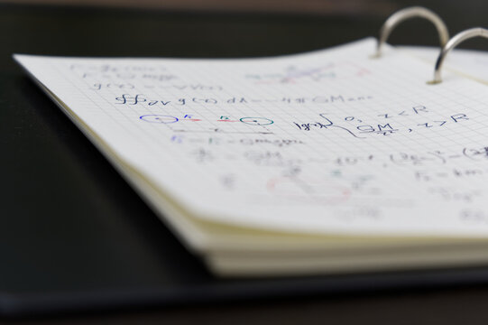 The image displays a notebook filled with complex mathematical equations and diagrams, written in blue and red ink, highlighting a detailed study or problem-solving session.
