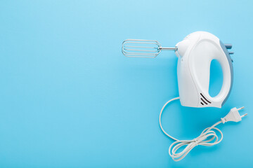 New white hand mixer with wire on light blue table background. Pastel color. Closeup. Kitchen electrical appliance. Empty place for text. Top down view.