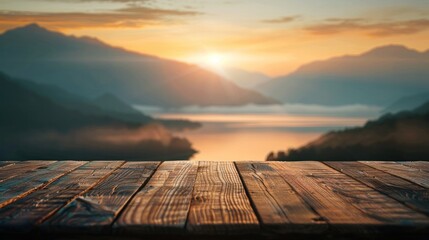 The top of a wooden table is empty with a blurred background of mountains and a lake at sunset with thin fog on the horizon - obrazy, fototapety, plakaty