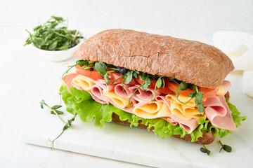 Sandwich. One fresh big submarine sandwich with ham, cheese, lettuce, tomatoes and microgreens on light background. Healthy breakfast theme concept, school lunch, breakfast or snack.