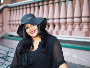 A Southern Asian plus size woman sits on a train platform looking at the camera.