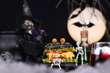 Monster Burger. Black bun, juicy beef cutlet, lettuce, onion, tomato and cheese in the shape of teeth, in the company of skeletons. Definitely a pick-me-up and a perfect Halloween party appetizer - obrazy, fototapety, plakaty