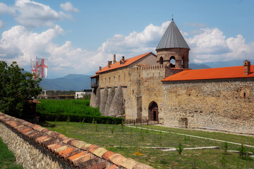 The grand stone Medieval Saint George church Alaverdi Monastery Complex with a striking red roof and tower stands tall against the sky, surrounded by lush green grass and plants