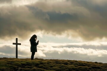 woman with folded hands praying before cross on a hill