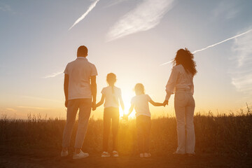 Happy family holding hands in field with plants at sunset. Concept of relationships and spending time in nature in evening, sunlight