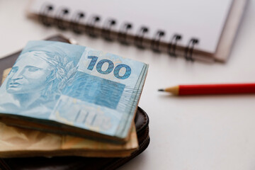 one hundred reais notes and other notes on the table with wallet, pencil and notebook