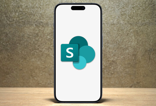 Microsoft Sharepoint logo is displayed on a modern smartphone standing on a wooden desk, collaboration Microsoft 365, team management, file sharing, organization, one drive, cloud