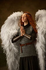 Red-haired maiden in angelic wings and medieval attire embodies a serene, prayerful stance against...
