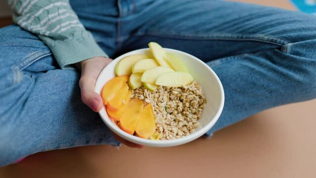 Top view plate with fresh fruits and muesli, unrecognizable woman eating breakfast