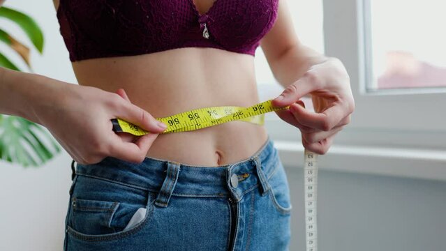 unrecognizable woman girl measuring her waist circumference with a tape measure
