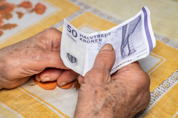 Old lady holds 50 Danish kroner in her hand, Denmark money, Cost of living in Denmark, Financial concept, Helping elderly people