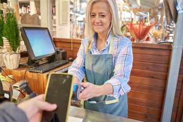 contactless mobile phone payment in a shop. middle-aged woman working as a cashier cashing up.