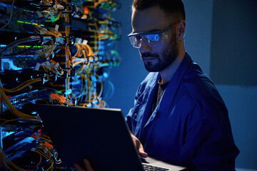 In glasses. Young man is working with internet equipment and wires in server room