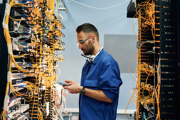 Professional device in hands. Young man is working with internet equipment and wires in server room