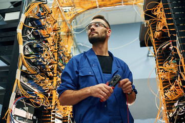 Administrator is busy. Young man is working with internet equipment and wires in server room