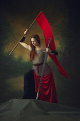 Spirit of insurrection. Redhaired princess with sword and red flag, posing defiant against vintage...