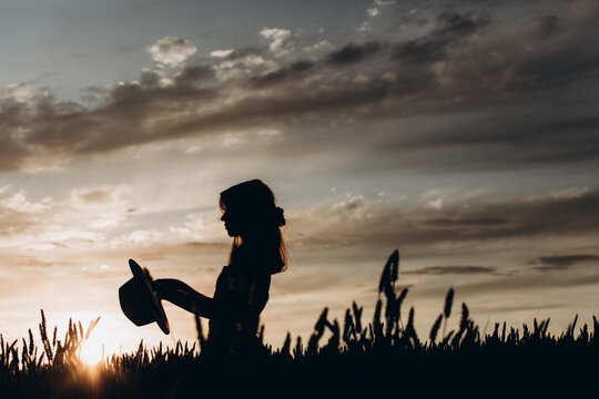 silhouette of a girl holding a hat at sunset in the field