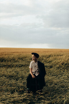 a village boy sits on a chair in the middle of a wheat field and looks away