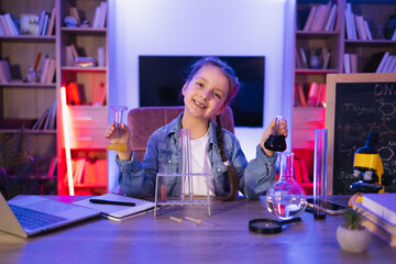 Small Caucasian girl scientist six years old in casual clothes sitting at table playing with...