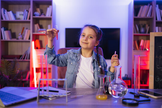 Science, hobbies, learning, education, discovery, childhood and domestic life. Focused Caucasian little girl doing chemistry experiment looking at test tube in evening at living room.