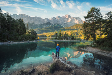 Man enjoying the amazing morning scenery at a gorgeous lake in the Bavarian Alps, with teal water reflecting the view of the mountain range and the nice clouds