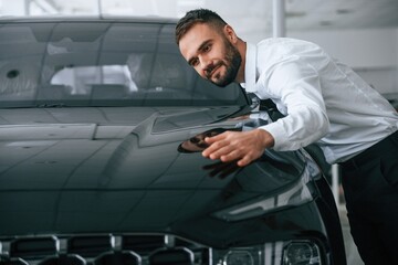 Embracing the car. Worker in formal clothes is in the auto salon