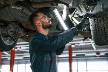 Under the vehicle, fixing. Car repairman is in the garage with automobile