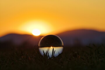 Glass sphere is silhouetted against a sunrise backdrop, warm orange hue radiating across the sky