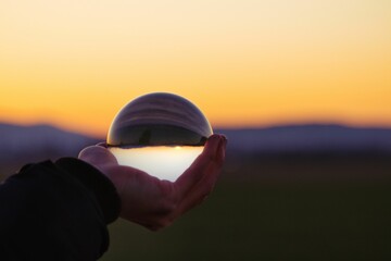 Silhouetted person standing in front of a breathtaking sunset, holding a clear glass ball - Powered by Adobe
