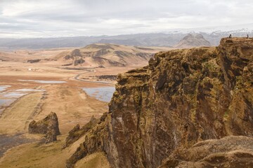 Rocky landscape just next to the black sand beach in Iceland with two ant-sized hikers on top of it