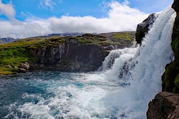 water falling down a rock into a river with green grass on either side