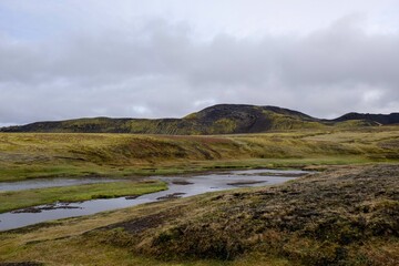 a small stream running through the grass land in iceland on a cloudy day