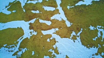 Aerial shot of the green field spotted with white snow