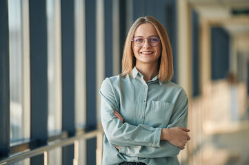 Smiling, standing with arms crossed, in glasses. Young woman in airport hall