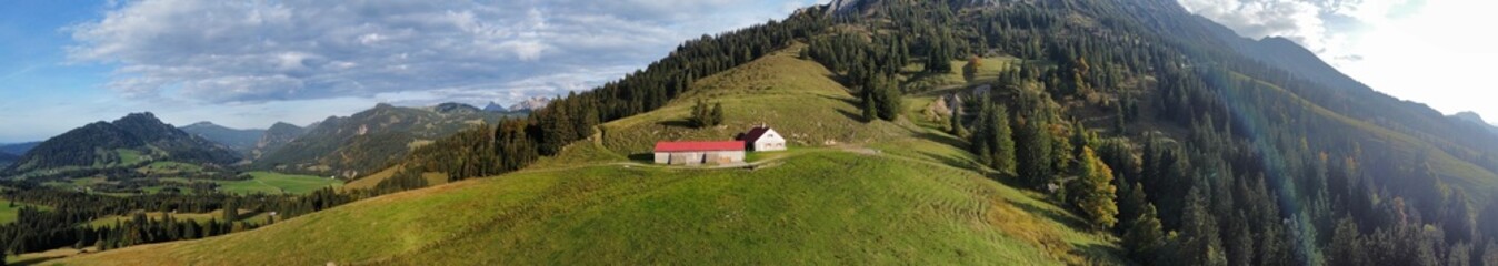 Panoramic shot of a small house on a lush green grassy field, with mountain range in the background