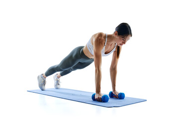 Young, fit, strong woman in legging and top doing push-ups with dumbbell pulls against white studio background. Concept of sport and recreation, movement, self care, action, energy. Ad