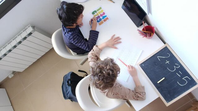 Two brothers sit together at the table, pencils scratching against paper as they tackle their homework. They lean in, heads close, discussing math problems and reading assignments.